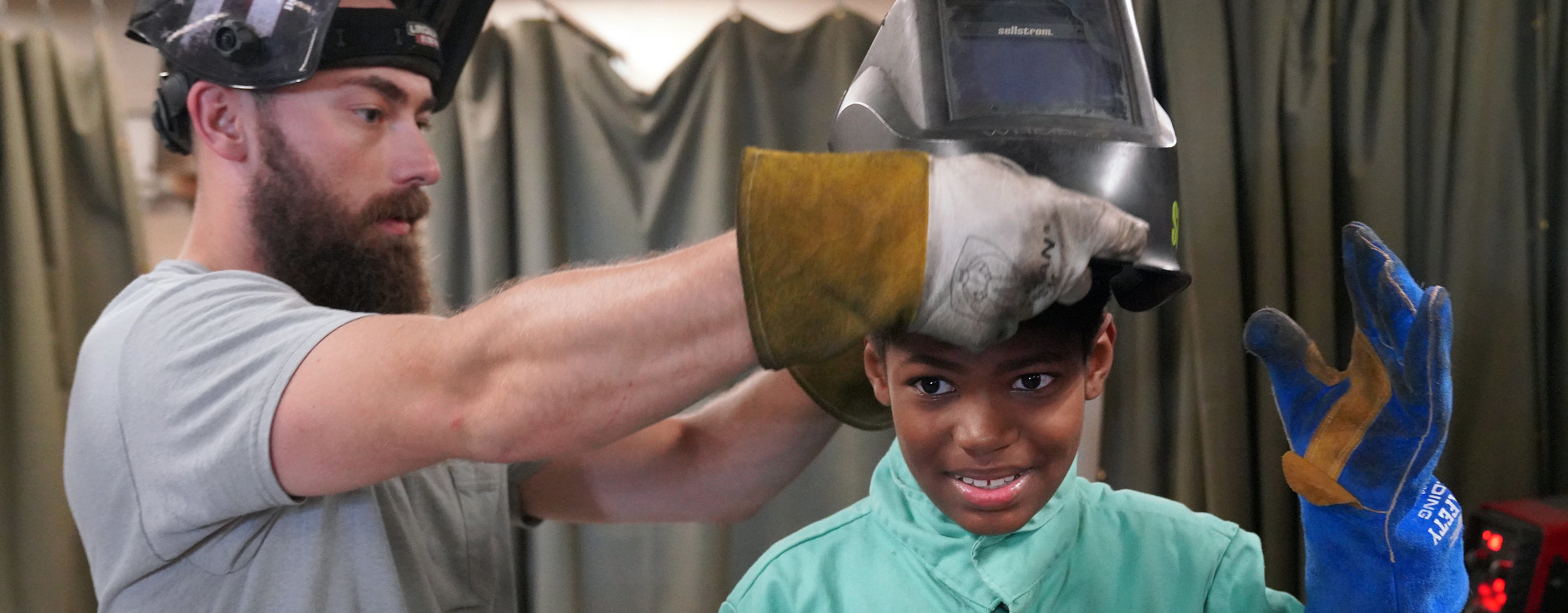 welding instructor putting a welding helmet on a child's head.