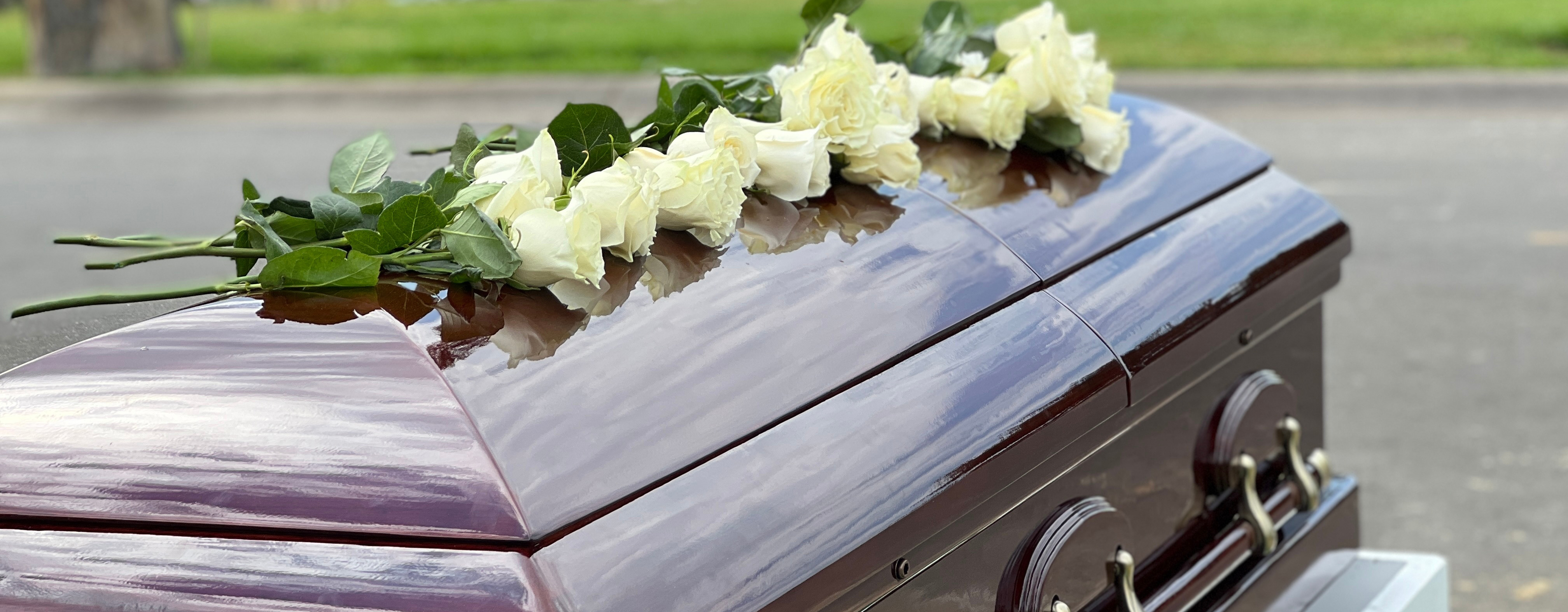 a casket with flowers on top if it in a cemetery.