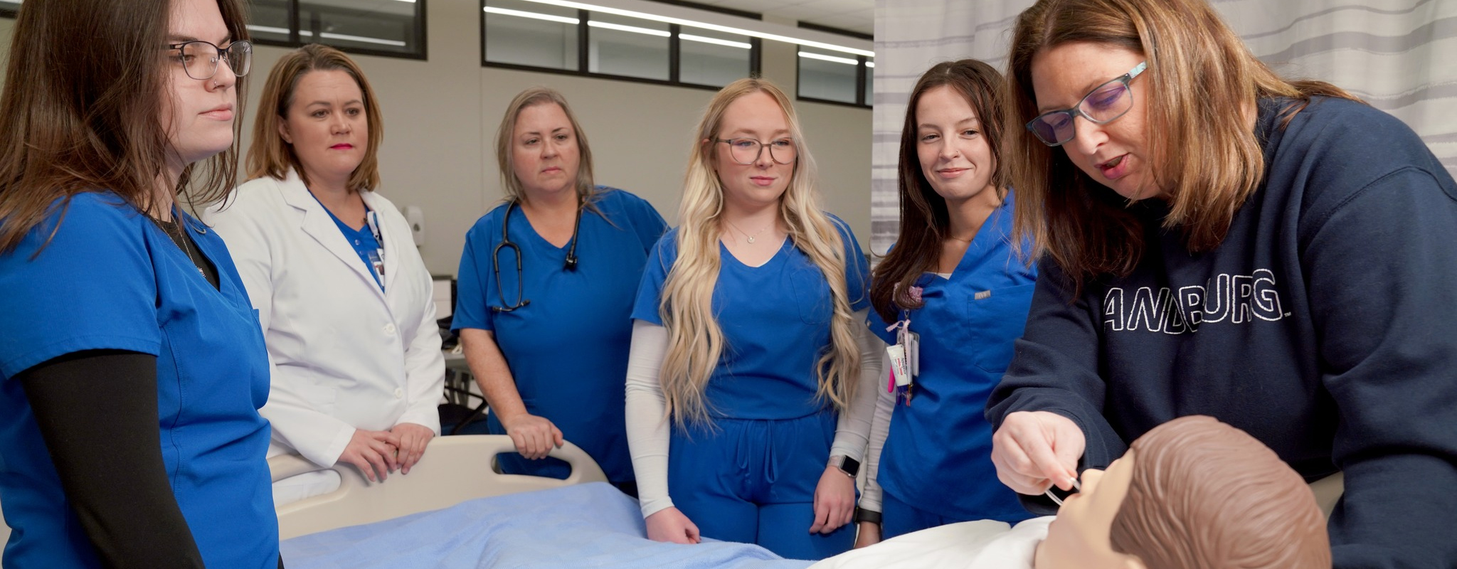 Nursing students watching instructor putting a tube in the nose of a dummy.