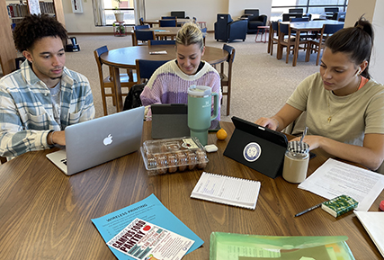 three people sitting at a table int he library.