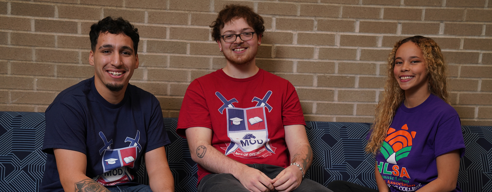 three students smiling sitting on a couch in a lounge.