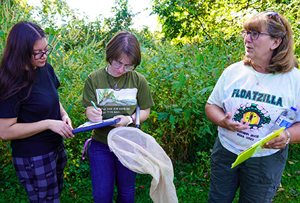 two students with instructor, talking about biology.