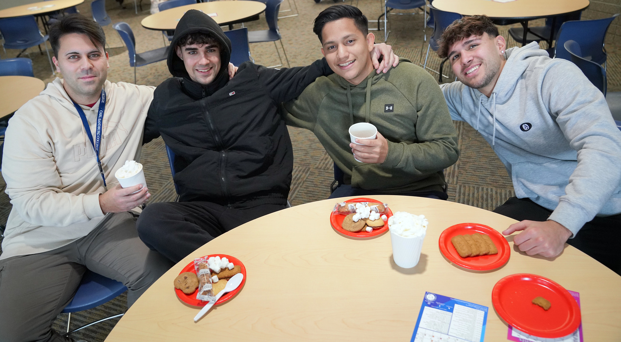 four male students sitting at a round table smiling.
