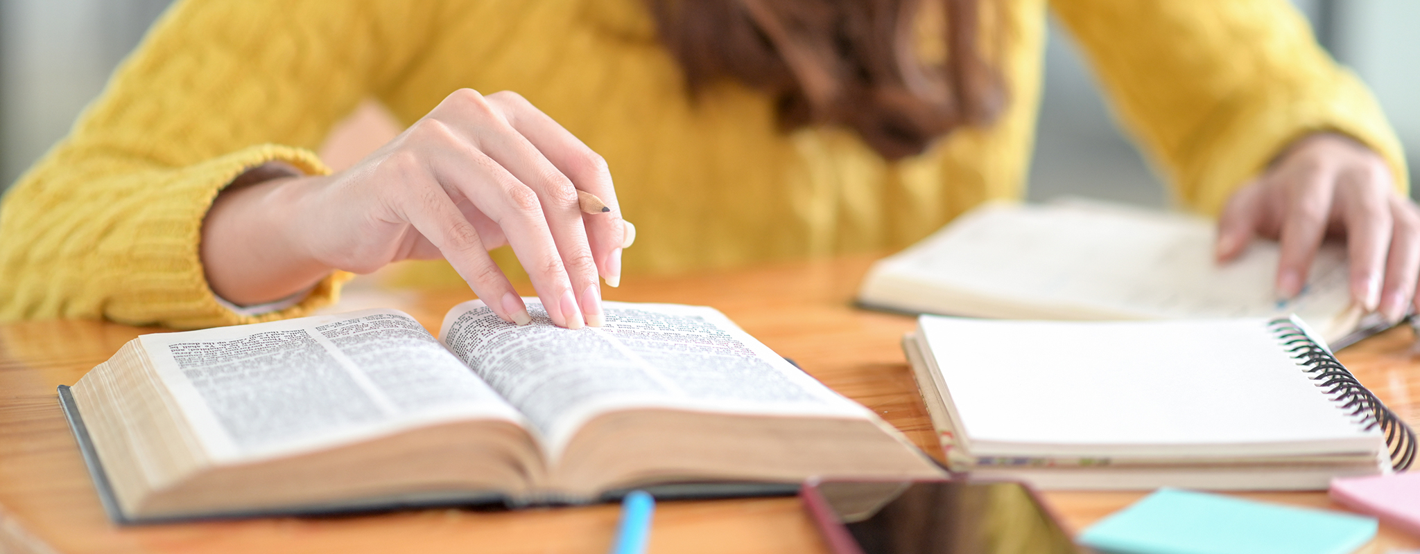 table with a book and notepad with a female holding a pencil about the book.