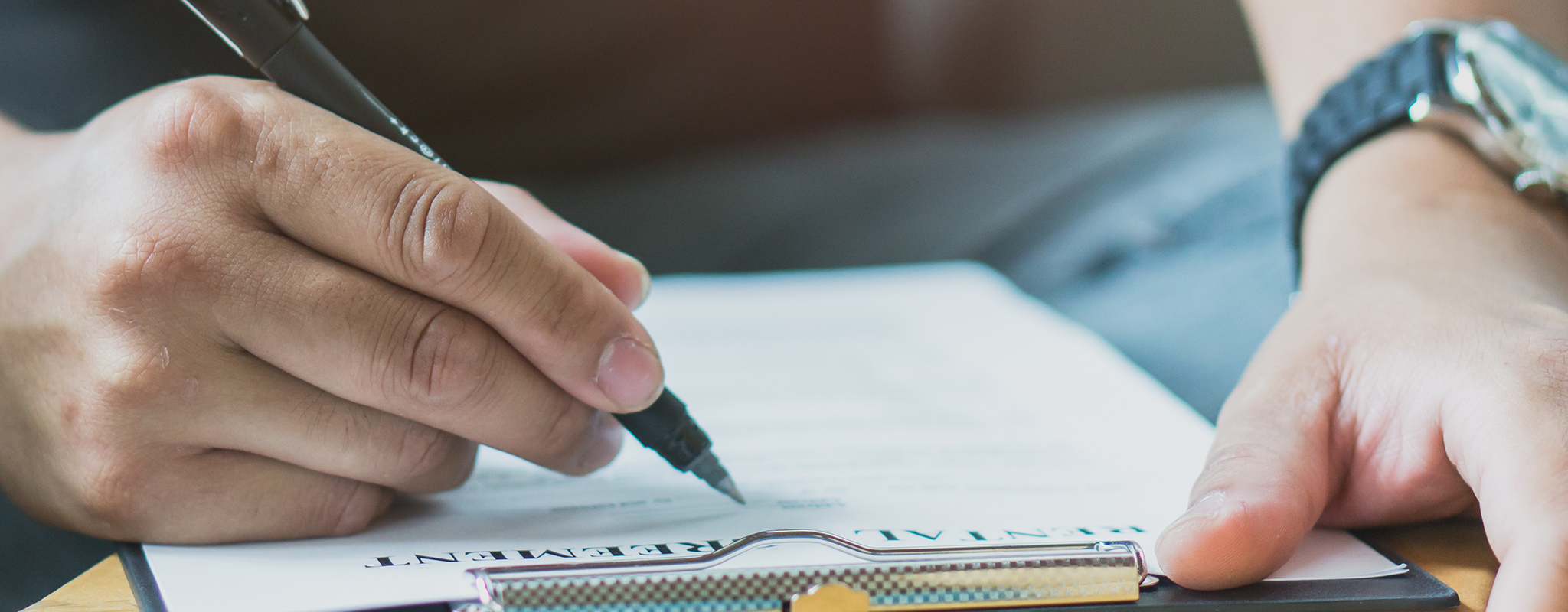 a person siting at a desk one of them has a pen and page filing a form out.
