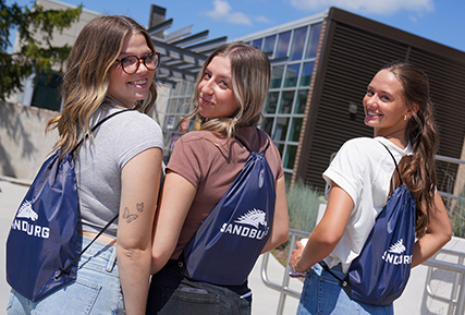 Three female students with Sandburg drawstring bags on their backs.